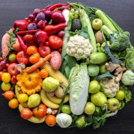 Various vegetables and fruits laid out in a circle on a dark background, top view.